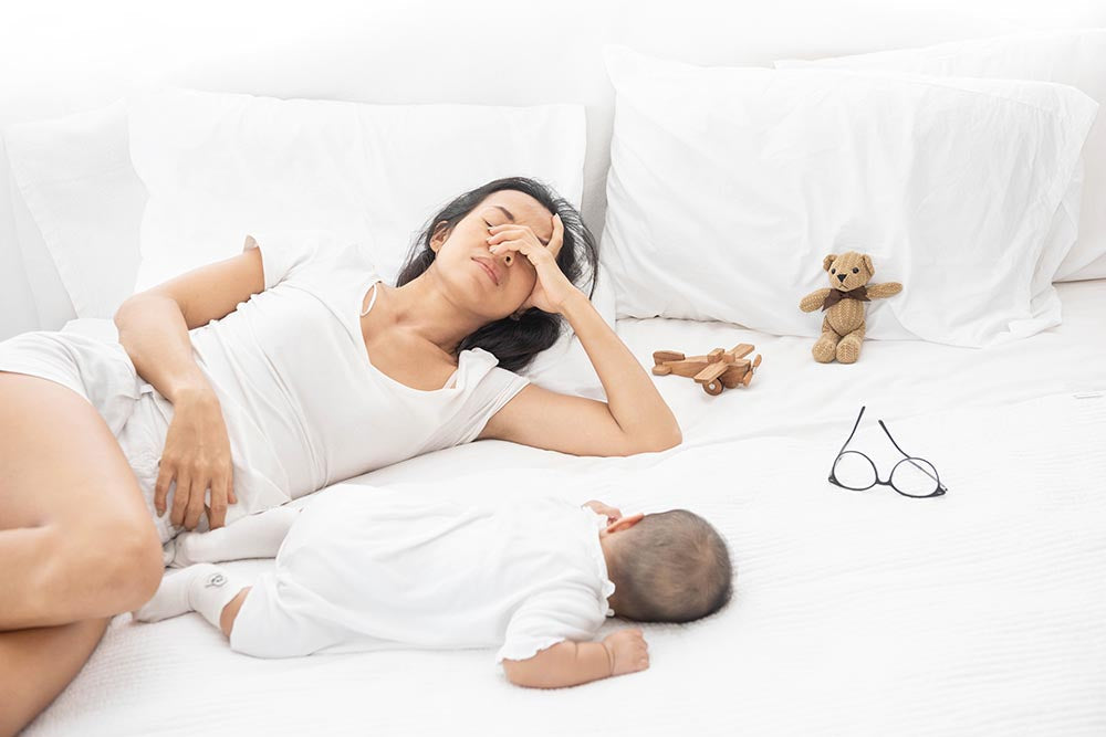 Mother resting with baby on bed, both looking calm