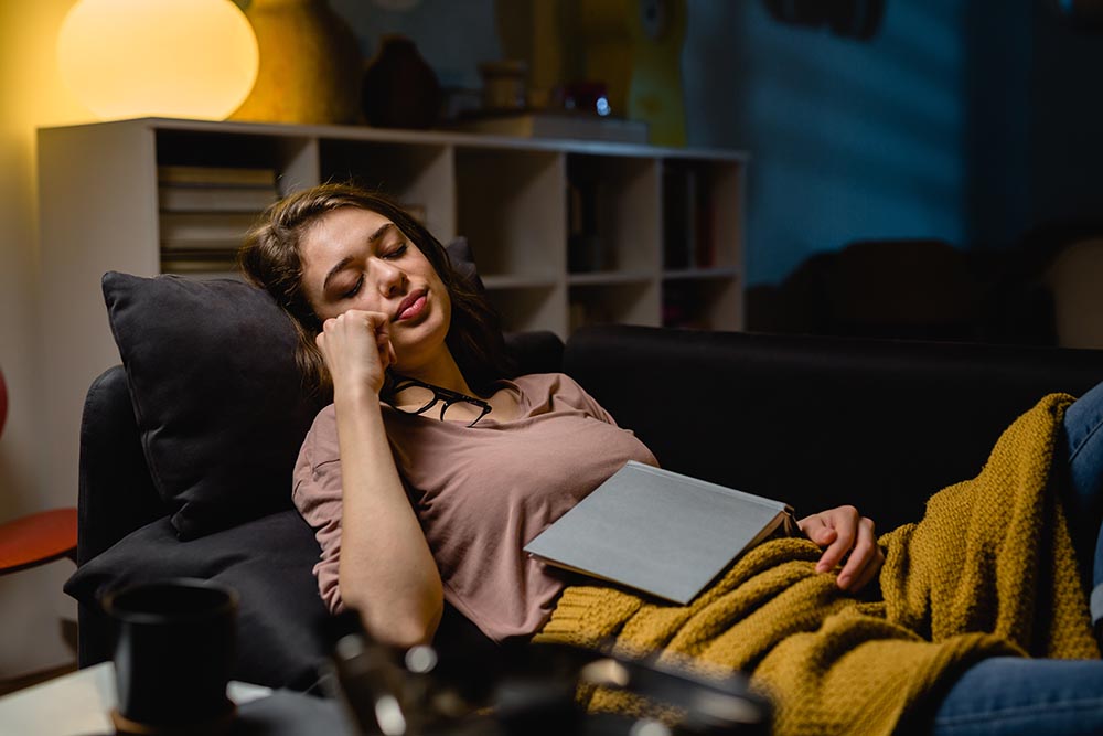Woman asleep holding book in chair how to sleep in a dorm room