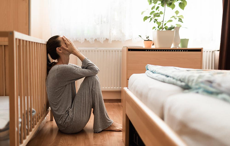 Woman sitting upset beside bed postpartum depression
