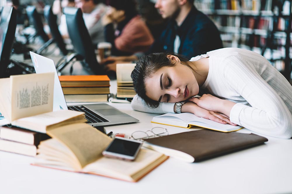how to sleep in a dorm room Student sleeping with books and laptop