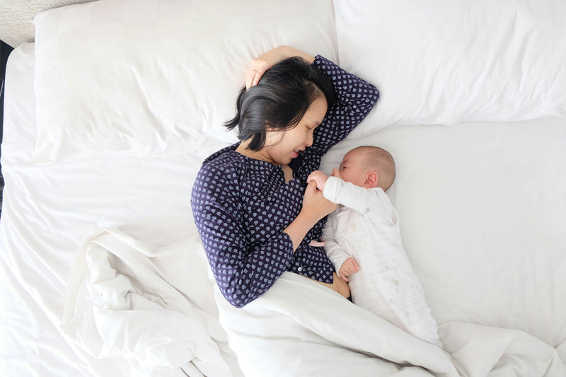 Mother resting with baby on bed postpartum fatigue
